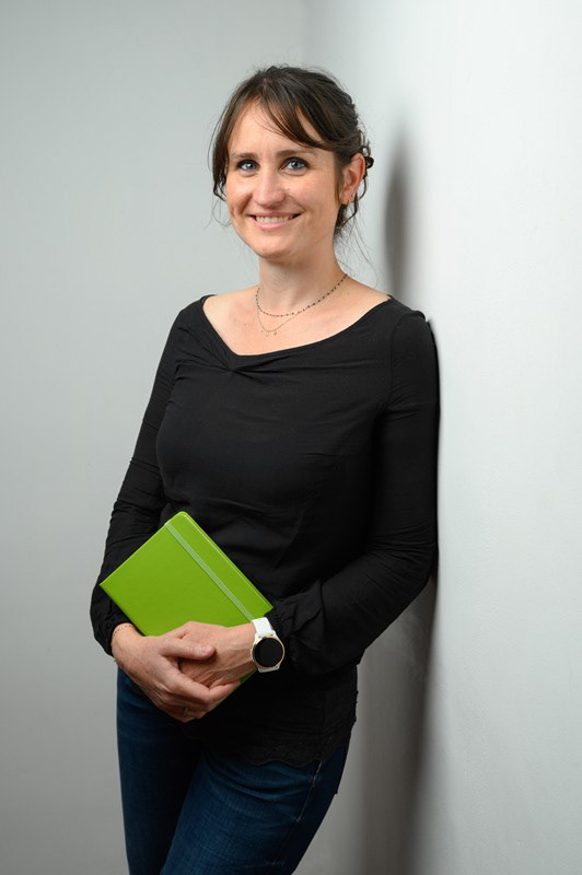 Portrait d’une femme tenant un carnet vert, sur fond clair